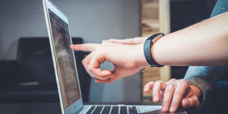 Two people pointing at a computer screen discussing the benefits of relationship mapping software.