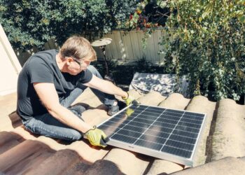 How to Choose the Best Solar Panel Installation Company 2 A man in black shirt sitting on the roof while holding a solar panel